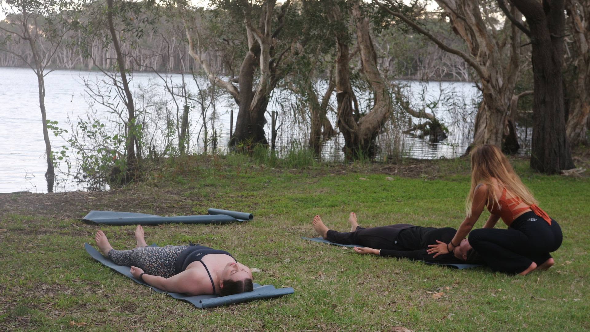 Nic guiding a group through savasana on the grass beside the lake