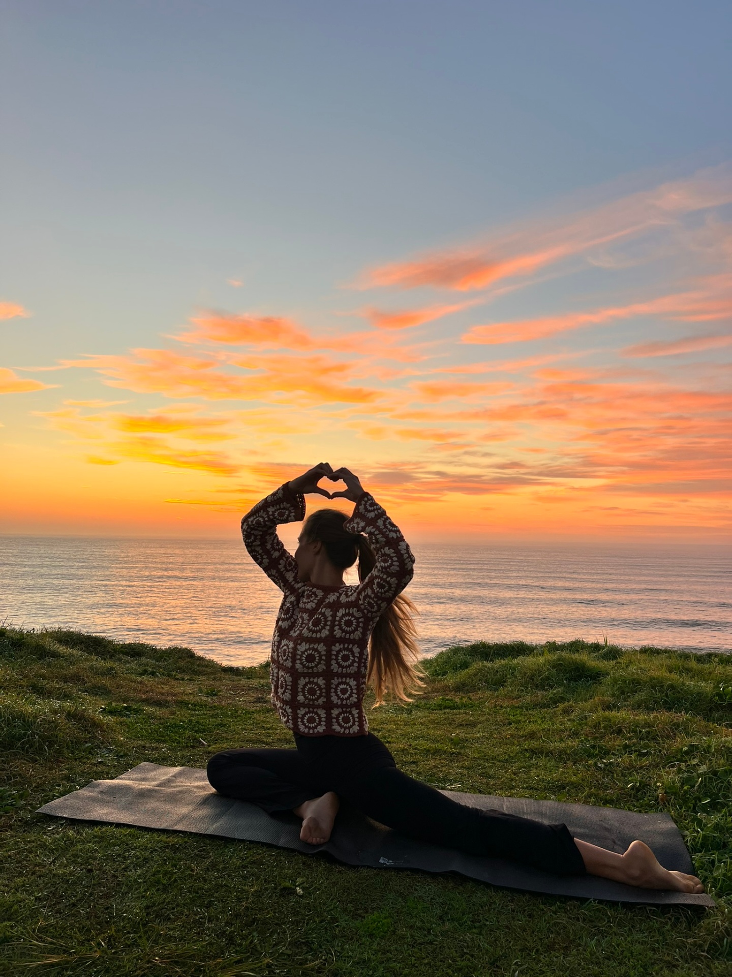 Nic in a seated heart-hands pose outdoors at sunset