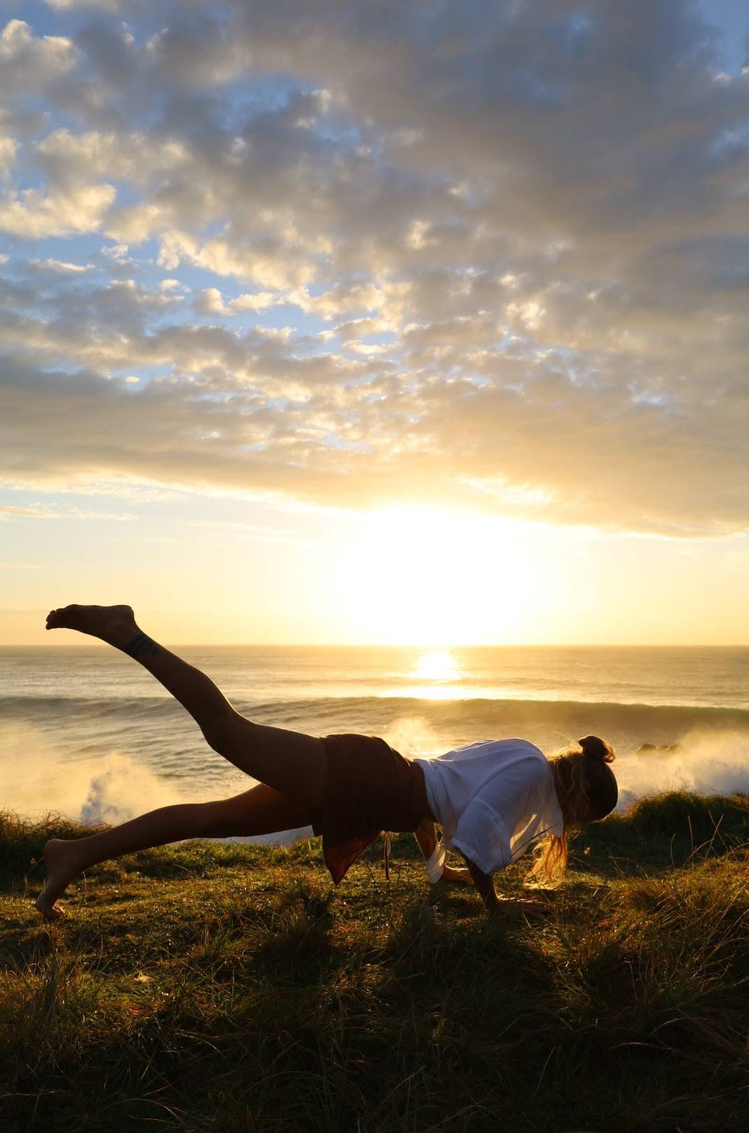 Nic in a plank with one leg lifted on a cliff at sunrise