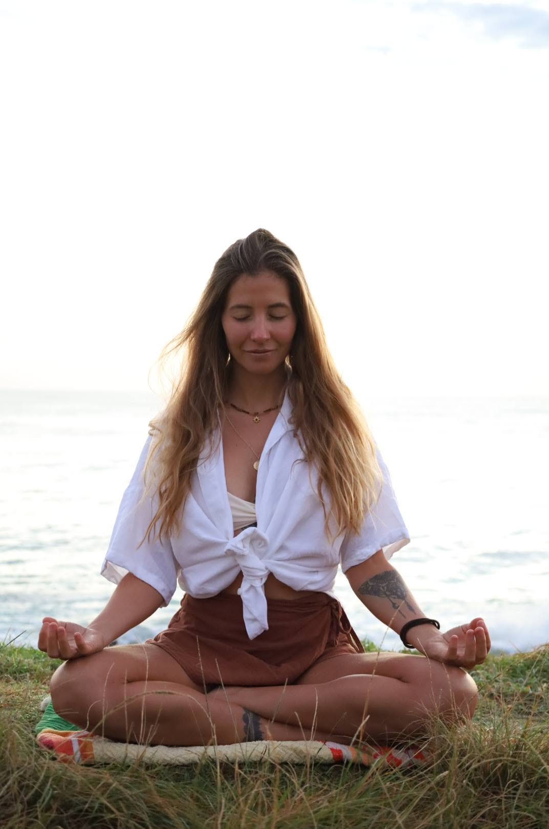 Nic meditating cross-legged on the grass by the ocean