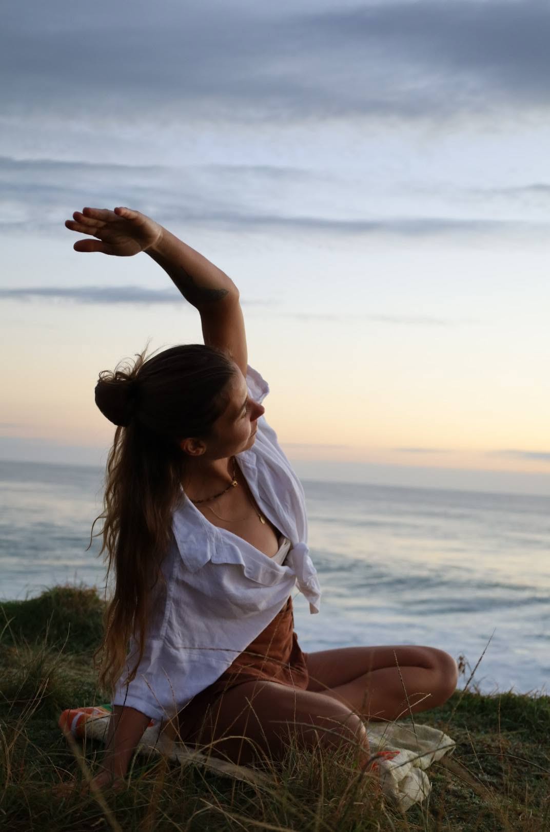 Nic in a seated side stretch on the grass overlooking the waves