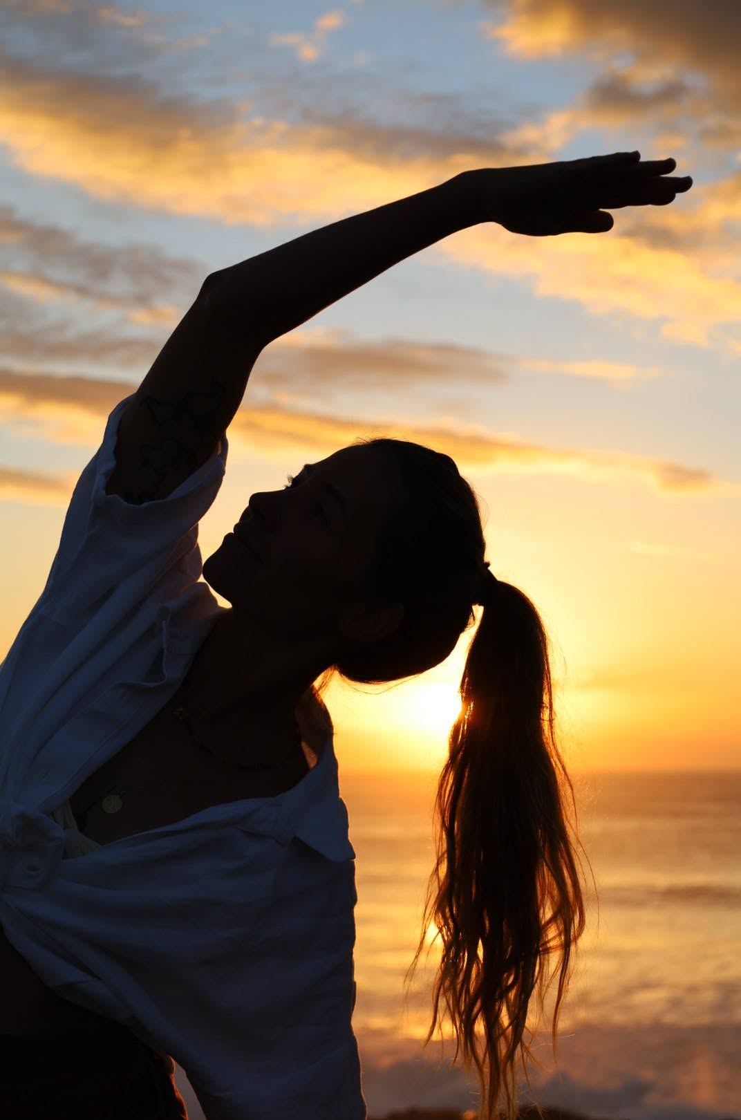 Nic in a seated side stretch silhouette against a golden sunset